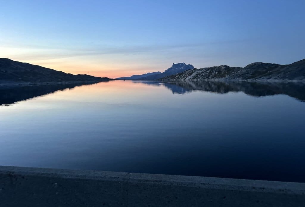 Um jovem confiante sai de um avião de hélice em Nuuk, Groenlândia, diante do parlamento nórdico sob um céu azul vibrante.
